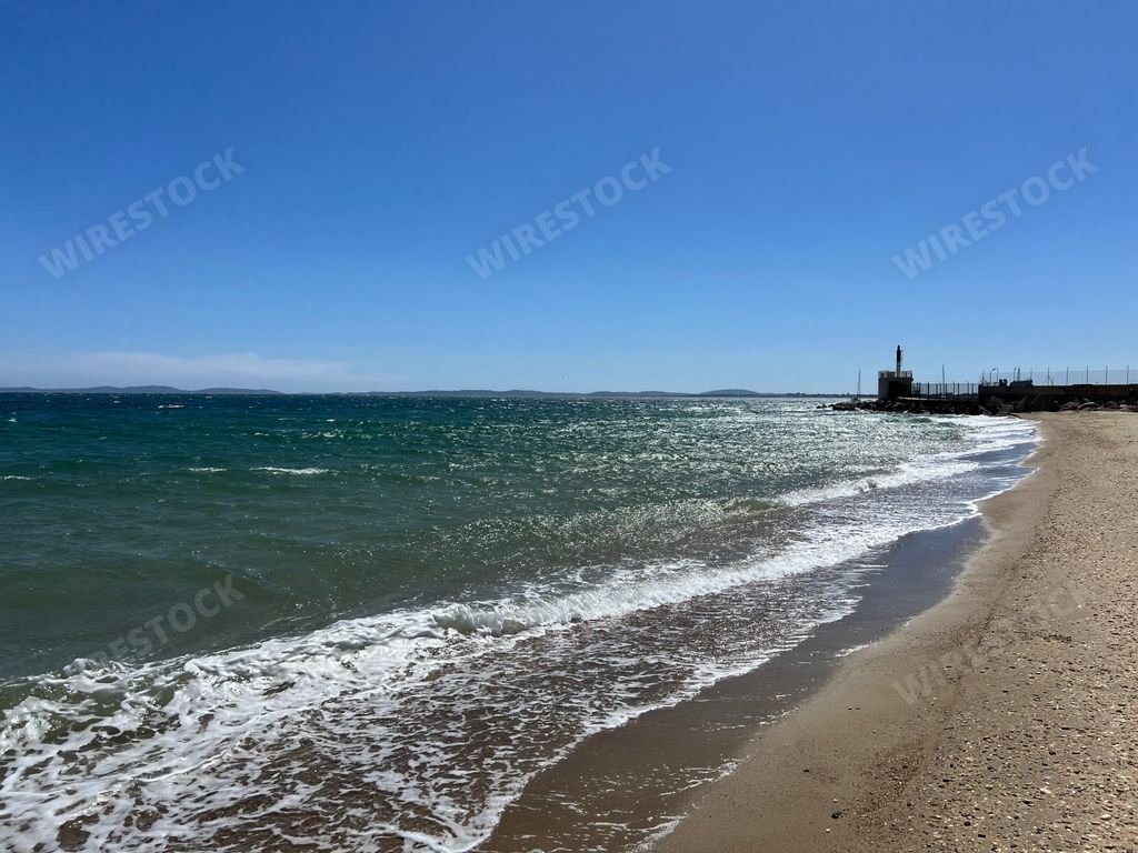 A serene beach scene with gentle waves and a clear blue sky, featuring a distant lighthouse