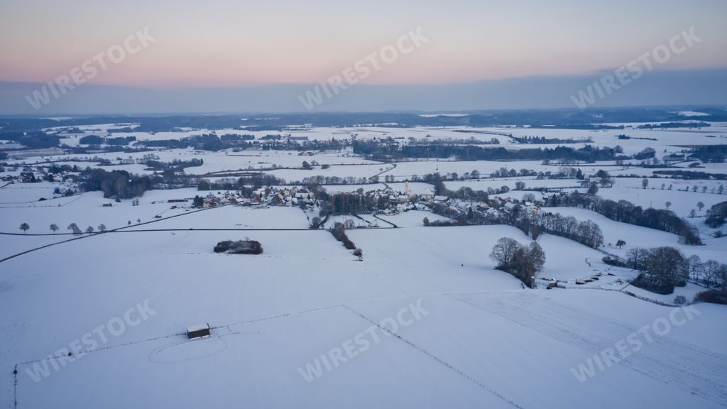 A chilling view of a snow-covered field in the countryside under a sunset sky