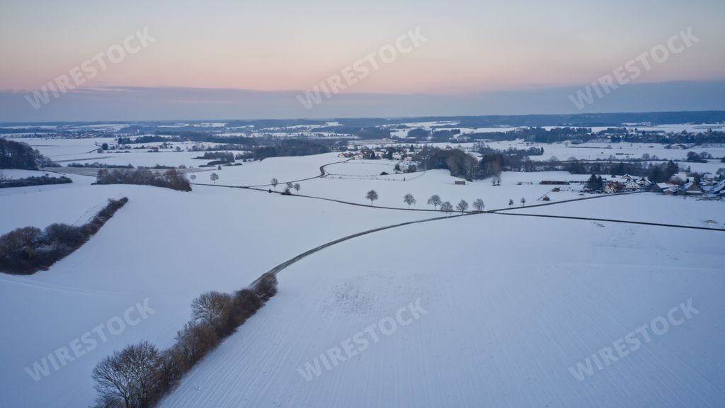 A chilling view of a snow-covered field in the countryside under a sunset sky