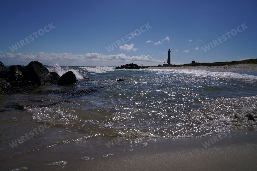 The sea waves touching the beach line with the lighthouse silhouette in the  background