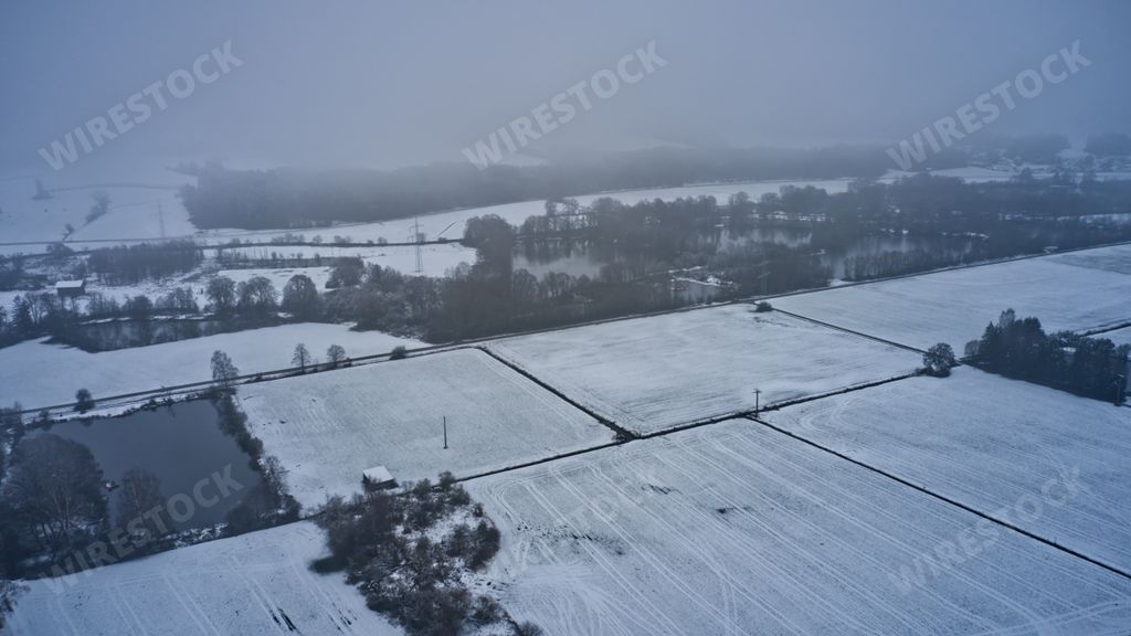 An aerial view of cultivated fields covered in snow on a foggy weather