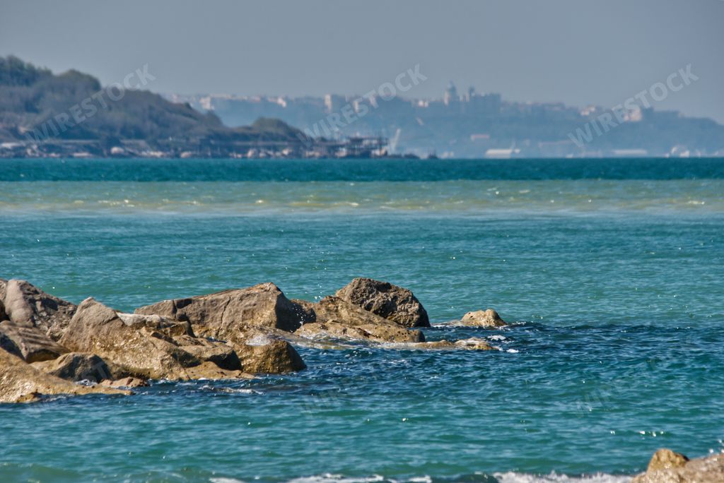 A beautiful rocky beach with a cityscape on the background in Italy