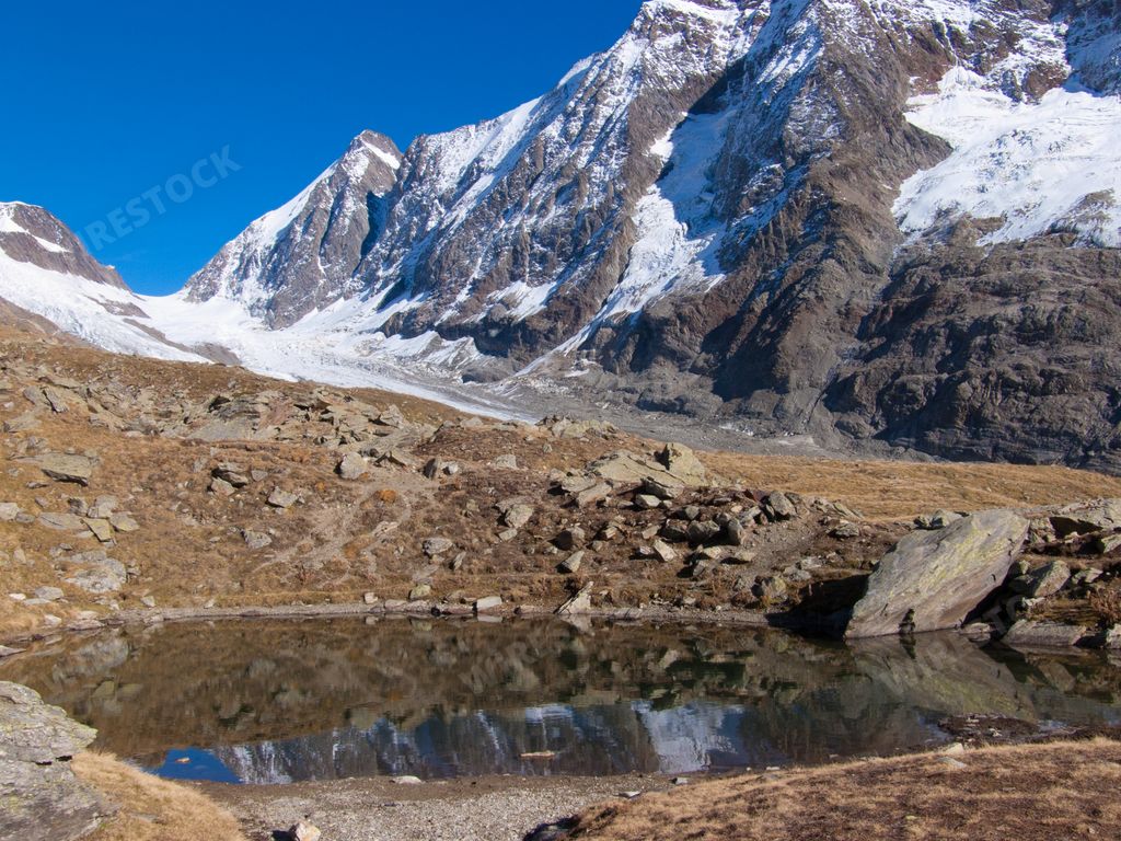 a photo of small pond against snowy mountain