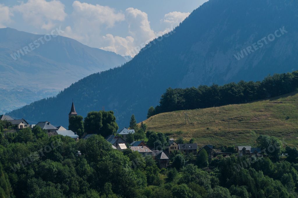 A scenic view of a village surrounded by green trees and hills against a mountain in Isere, France