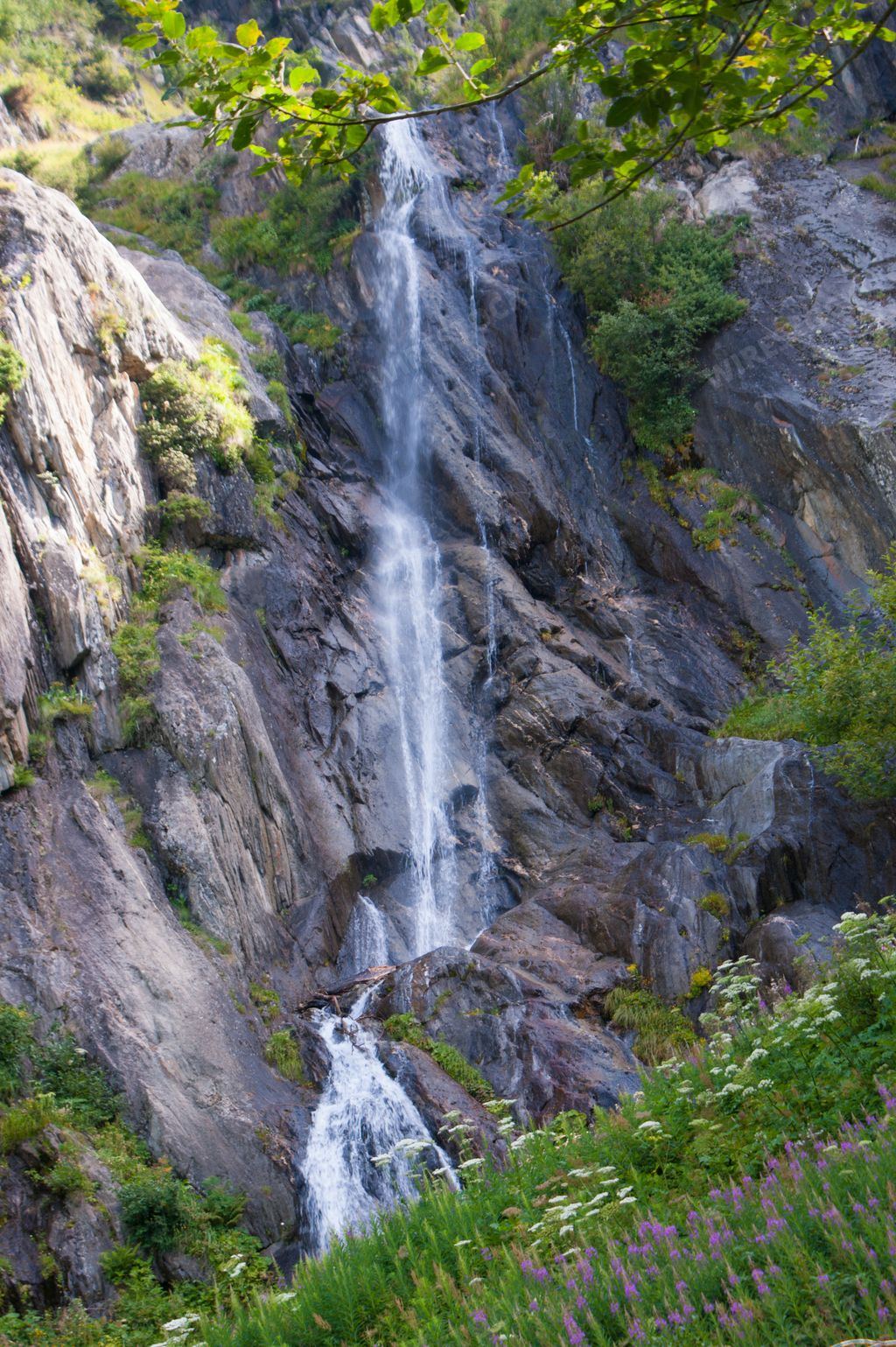 A vertical shot of a beautiful waterfall with a green field in Chamonix, France