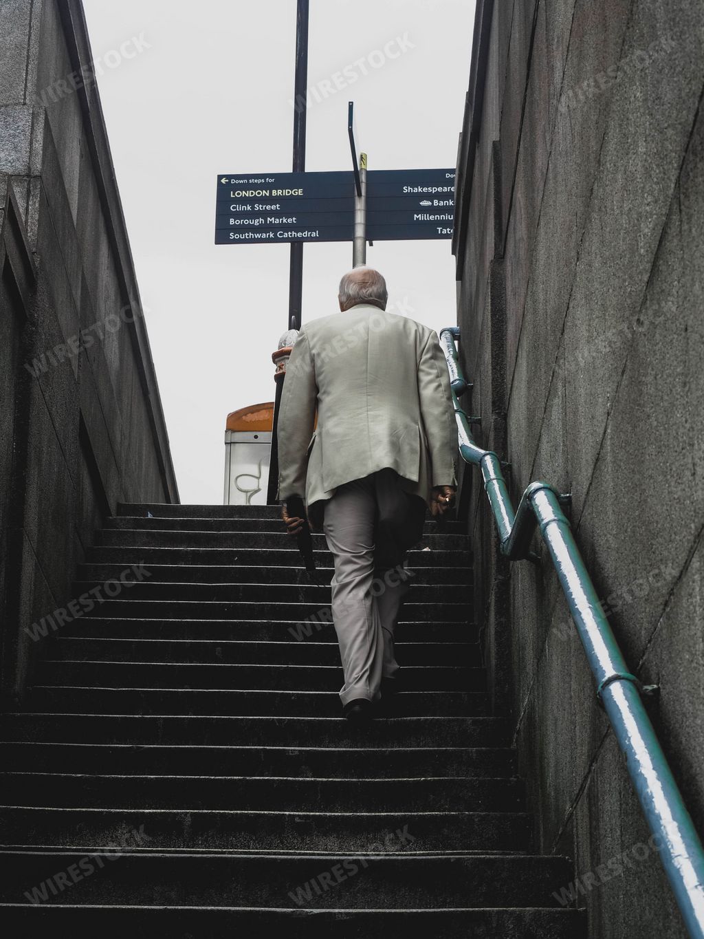 A vertical shot of a man in a suit from behind walking up the stairs in London