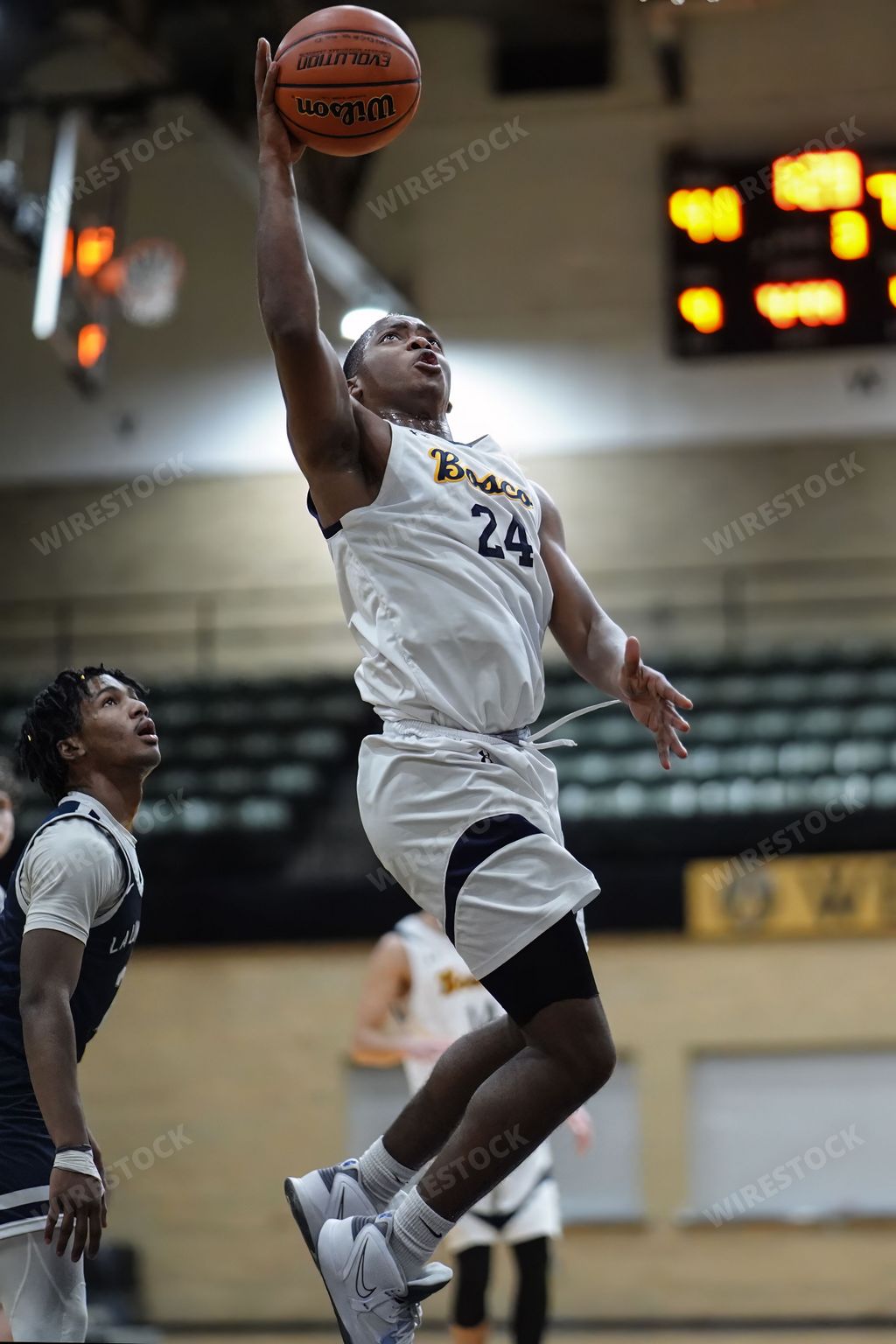 A man is dunking the basketball, while another person tries to block him