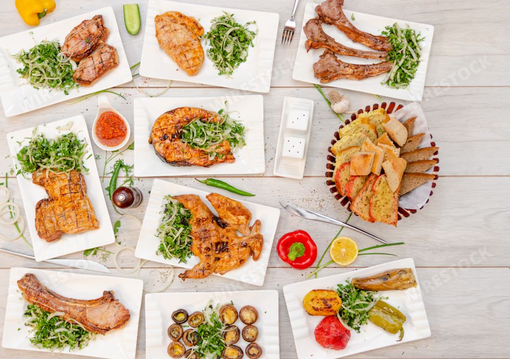 A top view of various types of meat dishes with cheese and a basket of bread on a wooden table