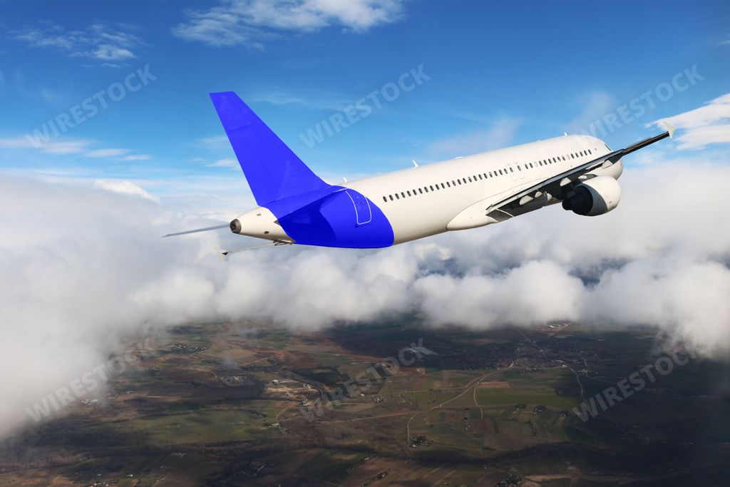 An airplane with a blue tail fin with clouds and a view of land under