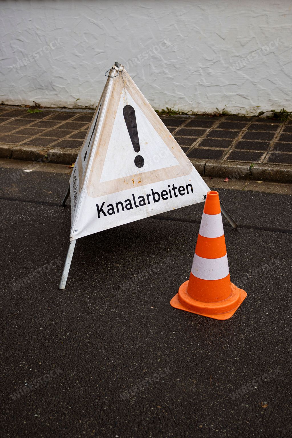 An isolated triangular warning sign with an exclamation point symbol in the center, set near an orange traffic cones