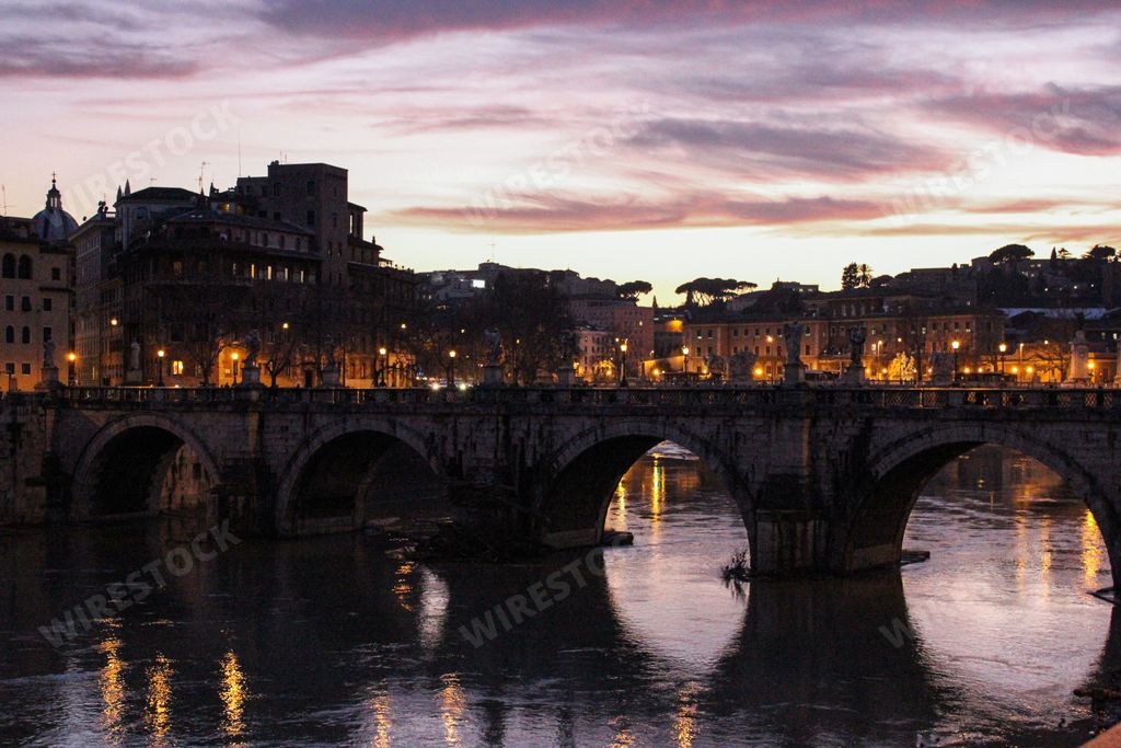A scenic view of an arcade bridge on Tiber River in Rome, Italy at pink sunset