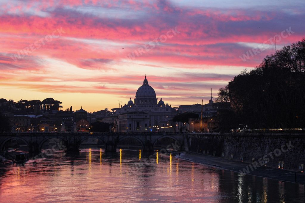 A scenic view of a bridge on Tiber River against St. Peter's Basilica in Rome, Italy at pink sunset