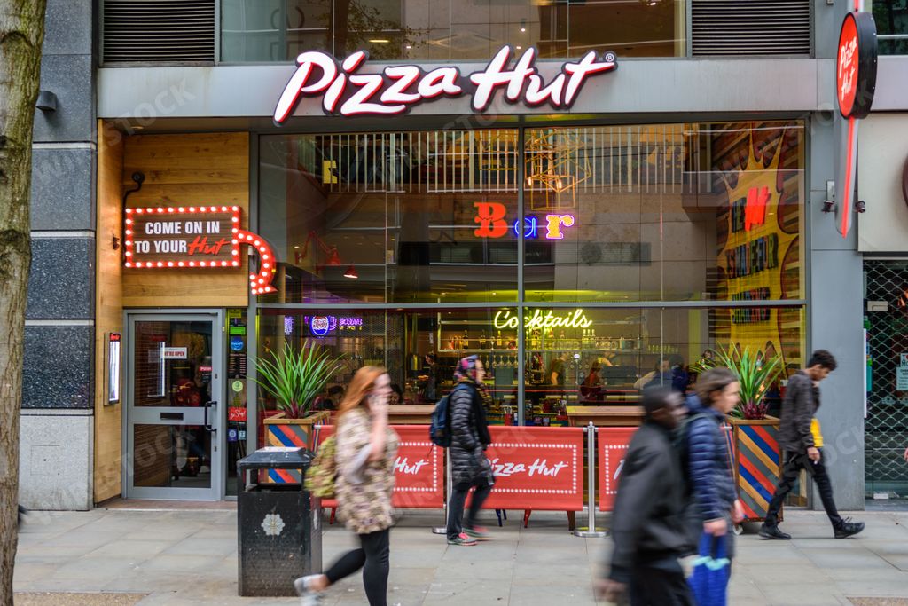 Shoppers and people pass by a Pizza Hut restaurant and take away on a busy high street in Manchester city centre.