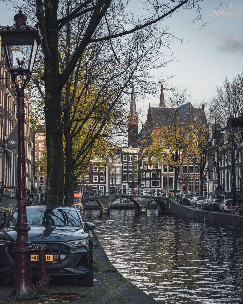 An autumn shot of Amsterdam, with canal, bridge, golden leaves, and the spires of De Krijtberg church.