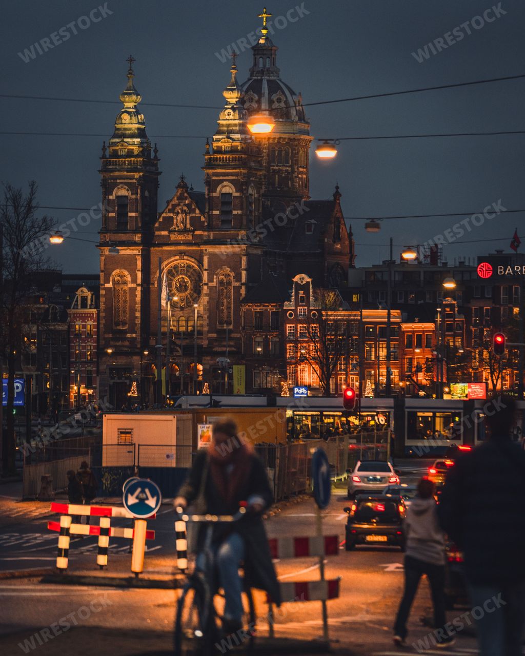 Amsterdam, Netherlands - November 27 2022: The Basilica of St Nicholas at night. A cyclist and tram pass by outside Centraal Station, in front of the