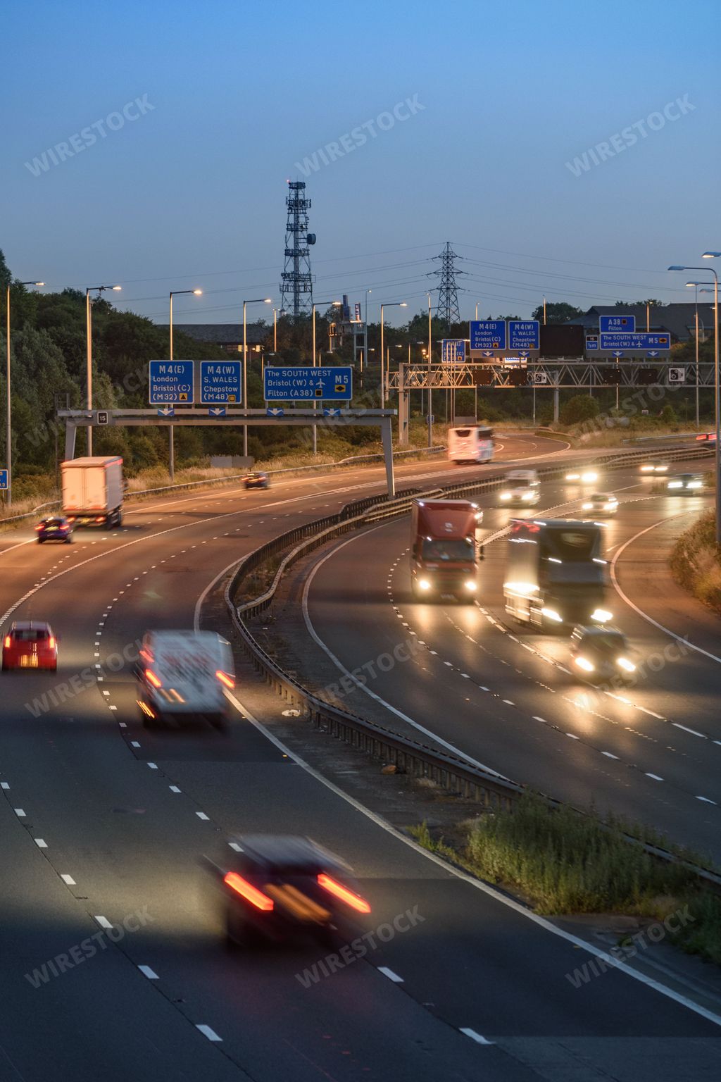 Vehicles move quickly past an intersection on the M5 motorway near Bristol, UK during the early evening. Blurred lights and light trails show speed.