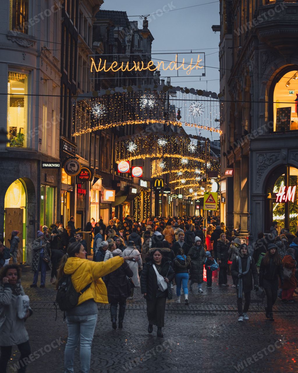 Shoppers pass down a busy street in Amsterdam, with Christmas lights during the festive period.