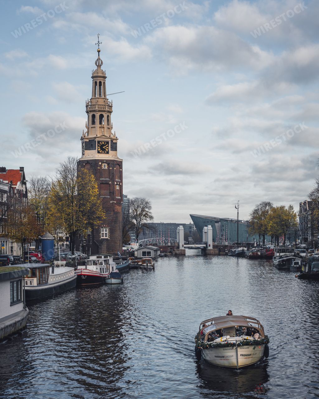 Amsterdam, Netherlands - November 28 2022: An autumn day in Amsterdam. A boat sails along a canal in the direction of Montelbaanstoren tower.