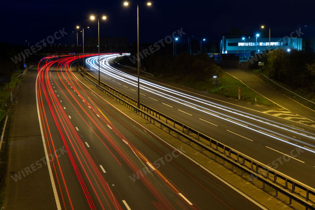 Fast moving traffic drives along the M5 motorway and highway road in UK. Light trails and streaks illustrate the illusion of speed using long exposure