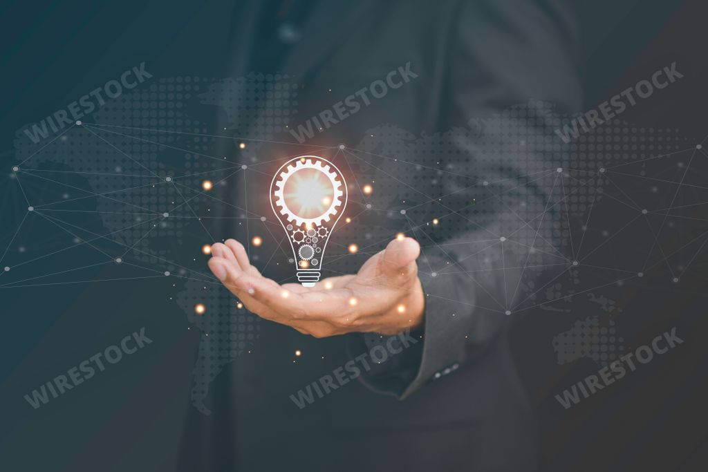 A man is holding an illuminated electric light bulb in his hand, offering it up to the viewer with a thoughtful expression