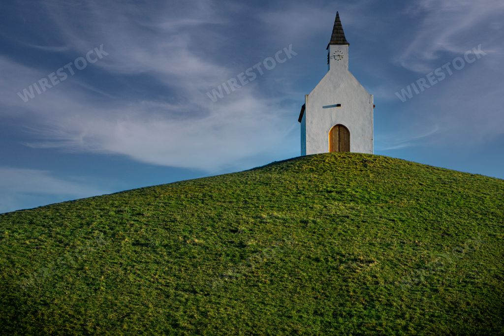 A low angle shot of a small church on a rural green hill in the Netherlands