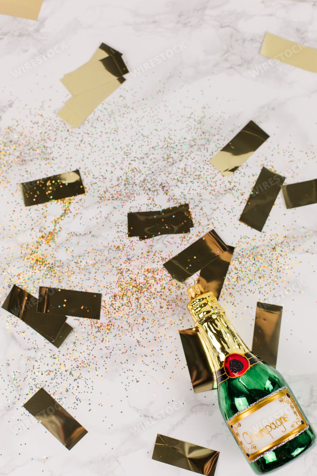 Christmas tree baubles in the shape of a green champagne bottle lying on a marble table. Glitter and golden stars decorate the picture.