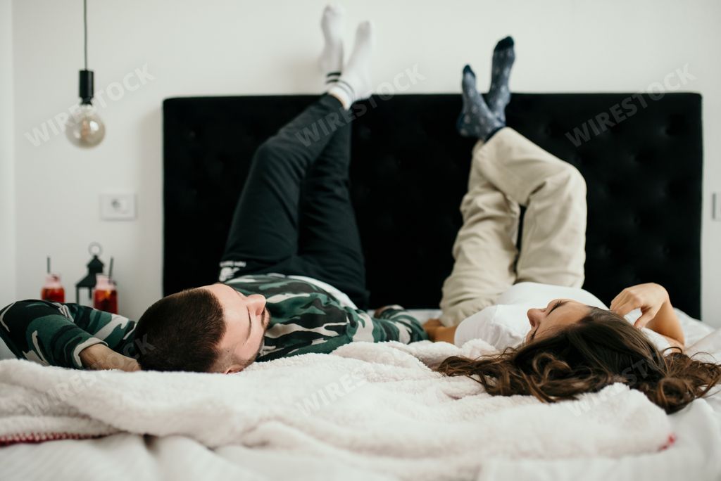 Young couple enjoying leisure time in bed, legs up in relaxed pose