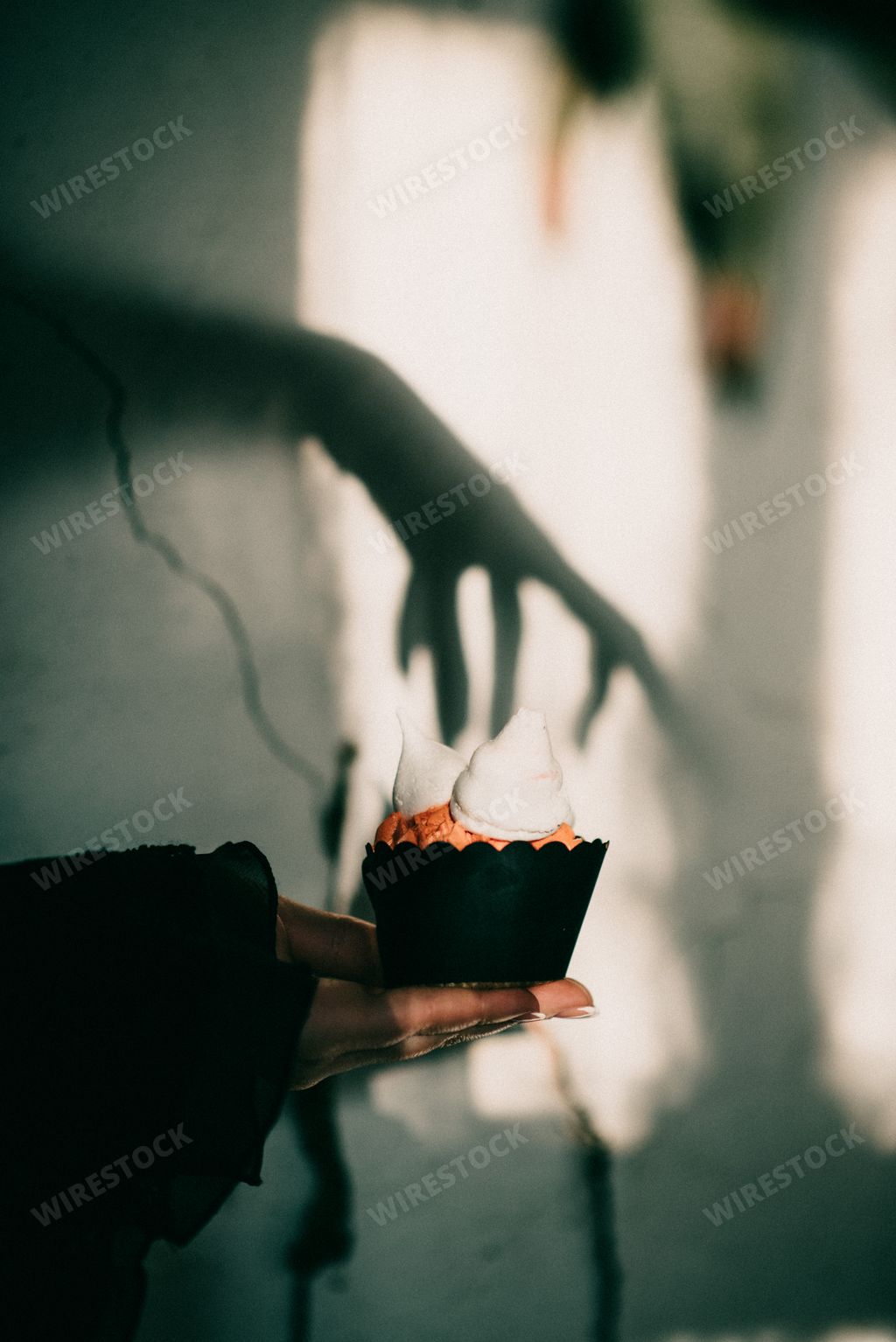 A vertical shot of a spooky Halloween setting, a cupcake with the shadow of a witch's hand above it