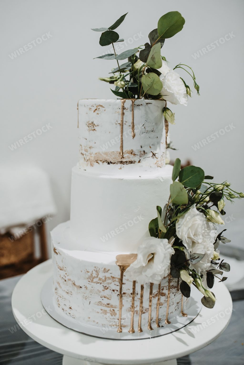 A vertical shot of a large wedding cake decorated with white roses and leaves