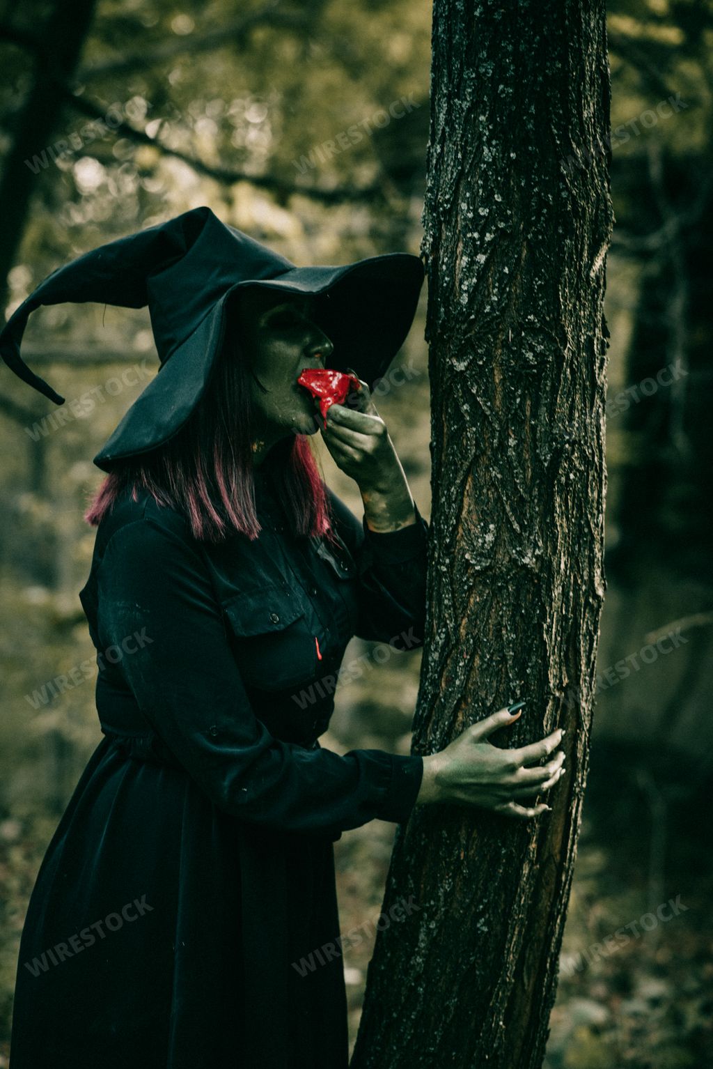 A vertical shot of a beautiful young witch with a Halloween costume eating in the garden
