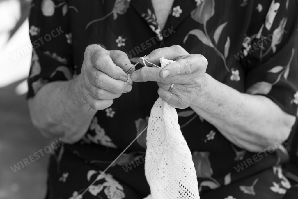 A close-up black and white shot of an old man knitting something