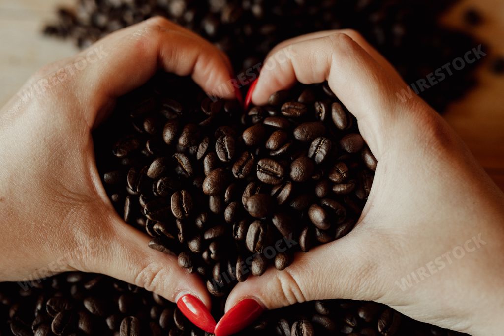 A woman's hand showing the heart gesture on the coffee beans