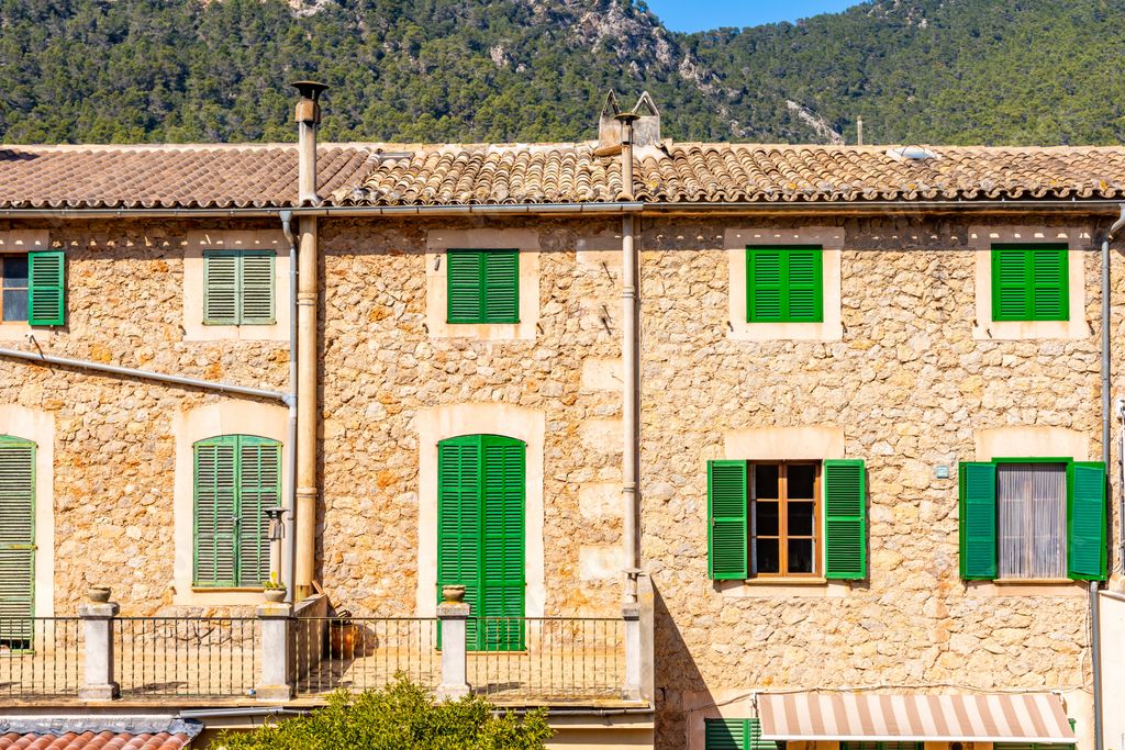 A view of a stony home with green windows in valldemossa, Mallorca, Spain on a sunny day