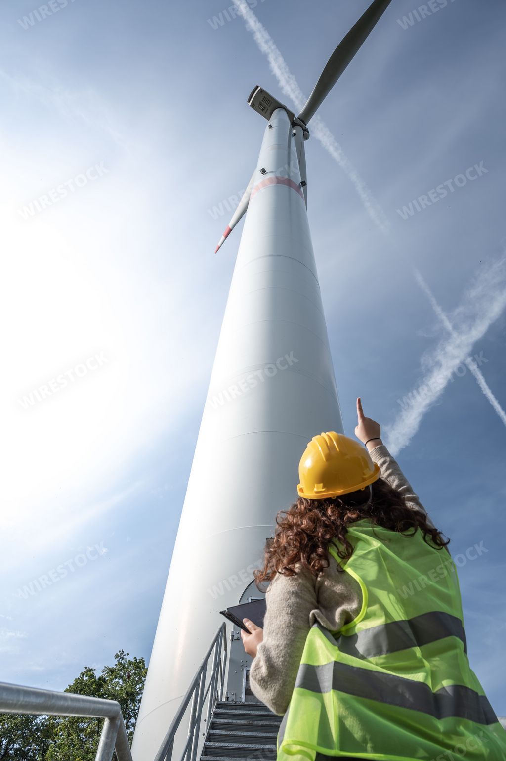A female professional wearing a hard hat standing and pointing to a windmill