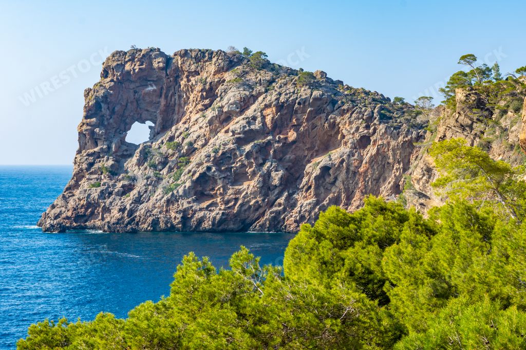 A view of rocky hill in the blue sea and green trees on a summer day in Majorca, Spain