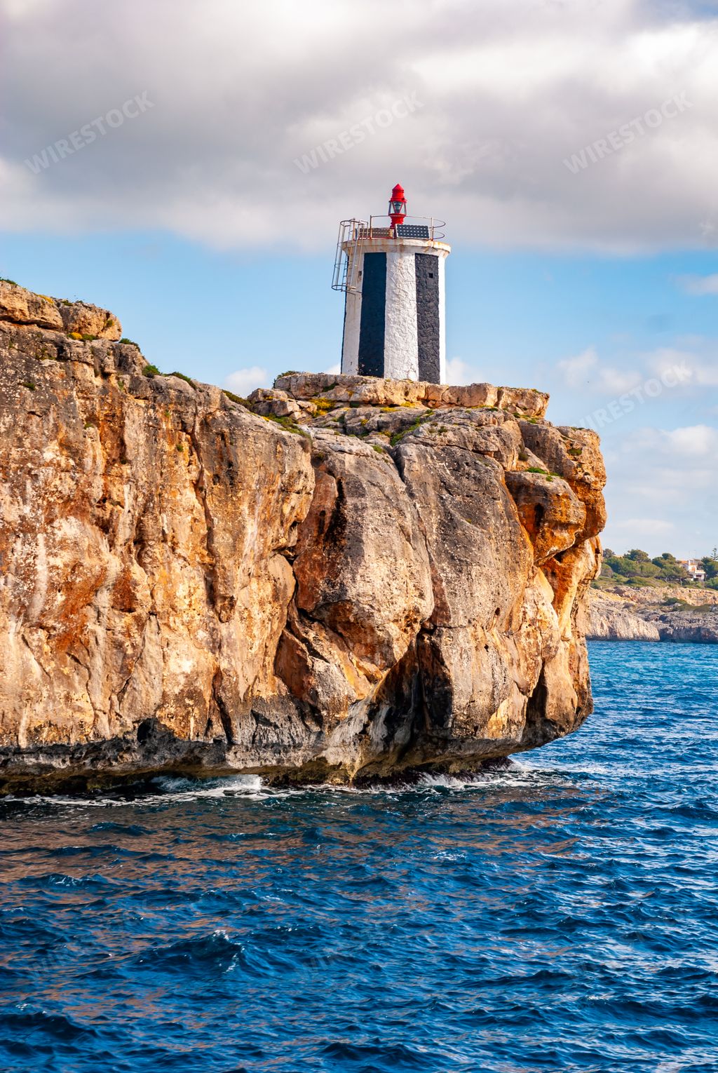 A vertical shot of a cliff with a lighthouse on it in Porto Cristo, Spain
