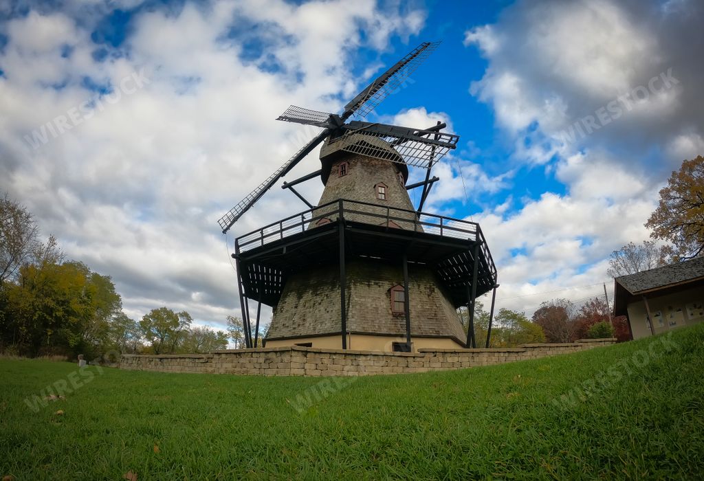 An old windmill on a farm field covered in greenery under a blue cloudy sky