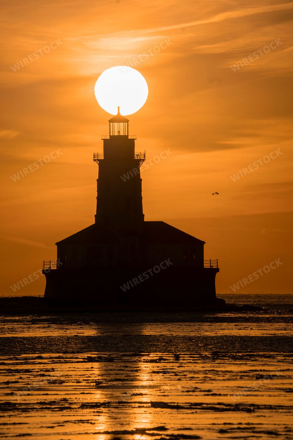 A peaceful orange and yellow sunset over a lighthouse in Chicago, with the sun setting on the horizon