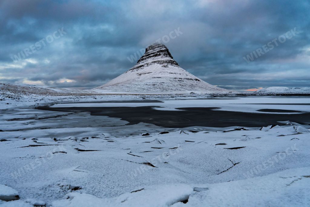 The Kirkjufell hill in Iceland with a frozen sea in front on a cold snowy winter day