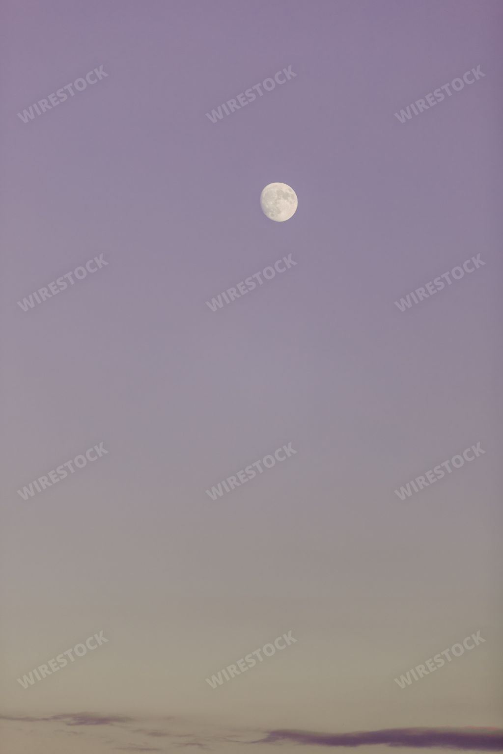 A beautiful night sky with a glowing full moon surrounded by a purple hue, and low clouds in the foreground