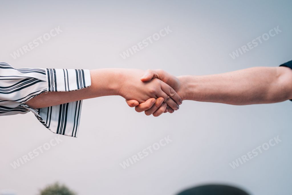 A male and female individuals shaking hands in a clear blue sky