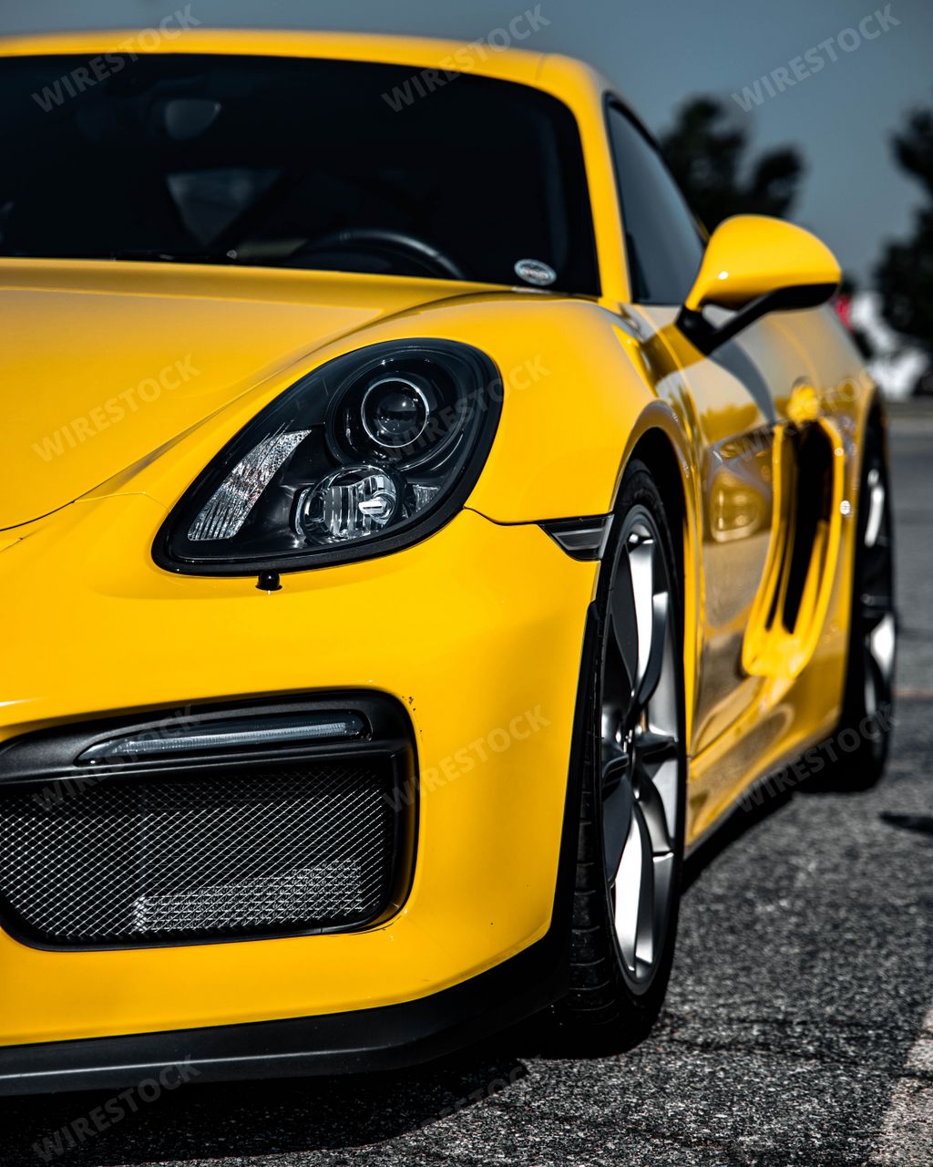 A vertical view of the front of a mesmerizing yellow Porsche Cayman sportscar outdoors