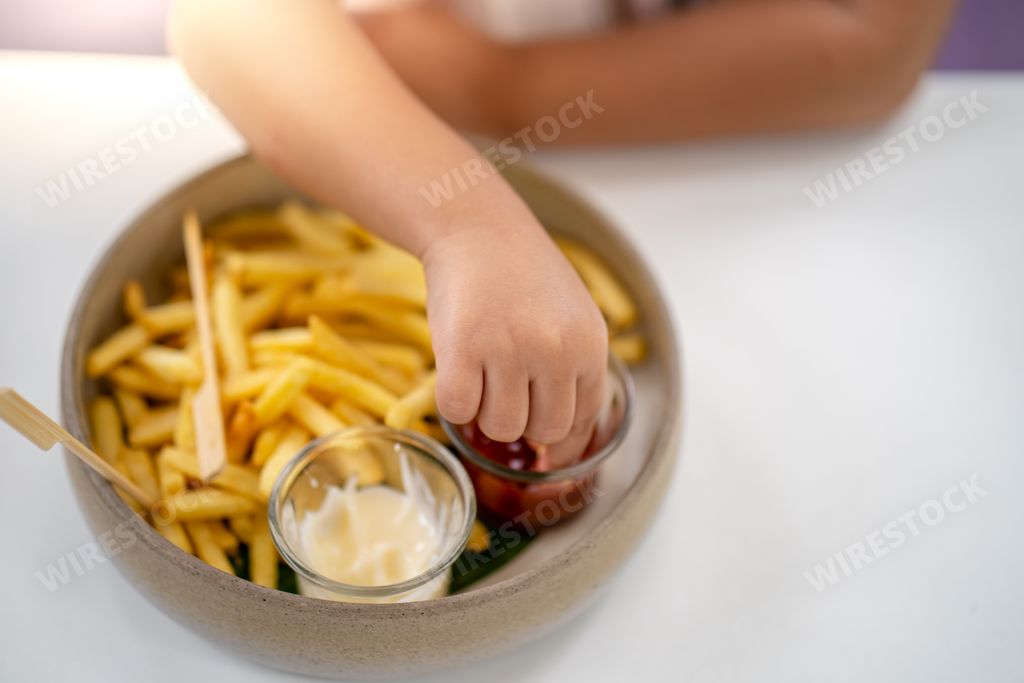 A person eating French fries with ketchup and mayonnaise