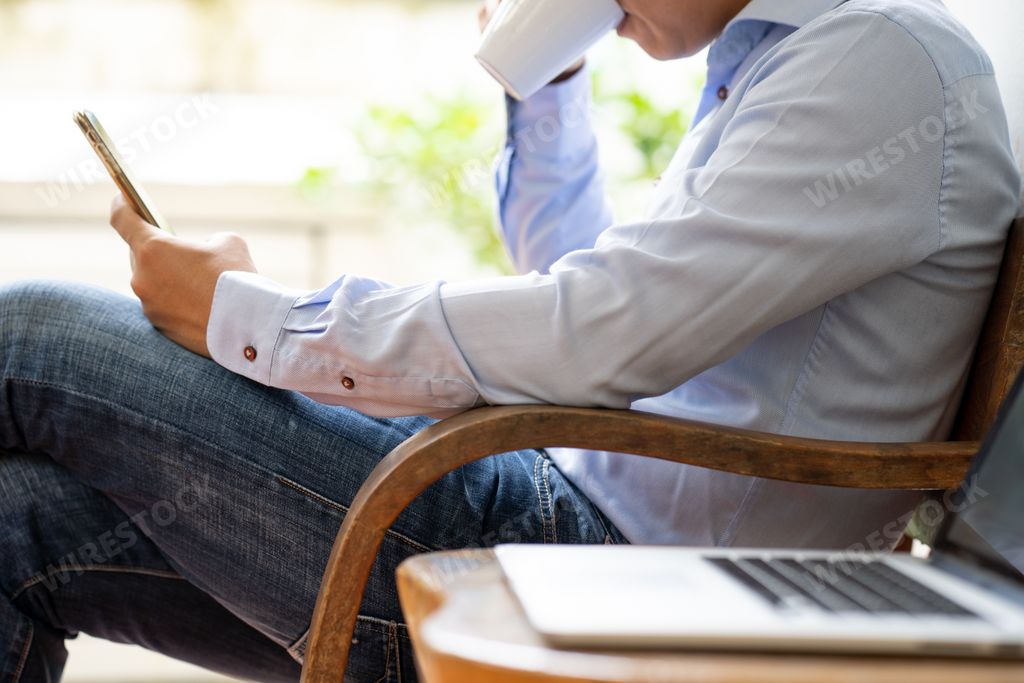 A closeup shot of a businessman drinking coffee while checking his phone in the office