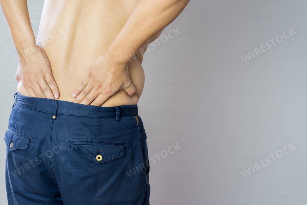 A half-naked Asian man standing and holding his back where he feels pain due to a back problem