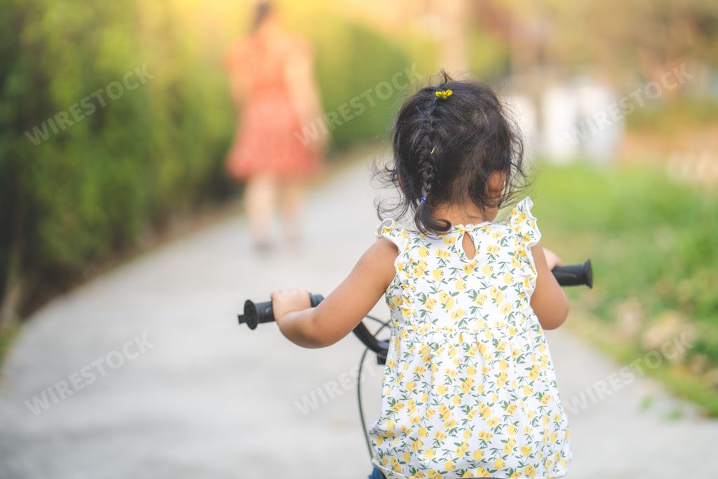A back view of a cute little Thai girl riding a bicycle in a park