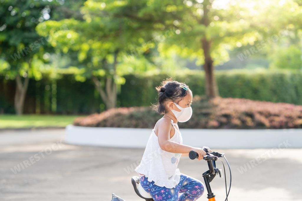 A cute little Thai girl riding a bike in a protective face mask