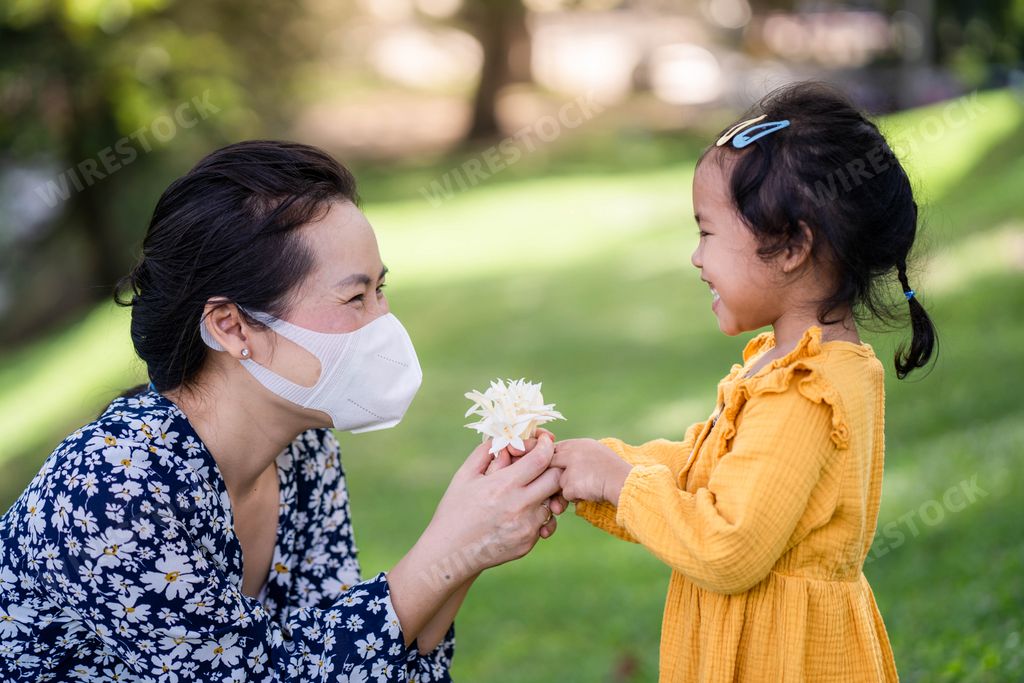 A cute happy Asian small girl giving her mother an Indian cork flower in a park