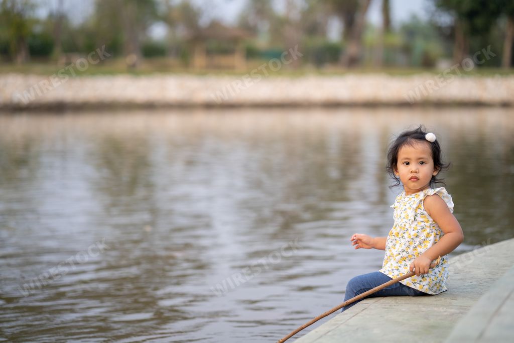 A cute little Thai girl sitting on the coast of a lake