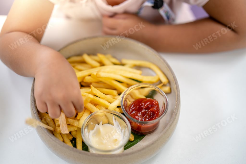 A person eating French fries with ketchup and mayonnaise